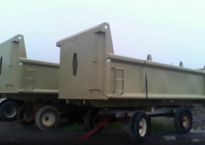 Two large olive/tan-colored steel dump truck bodies on wheeled trailers