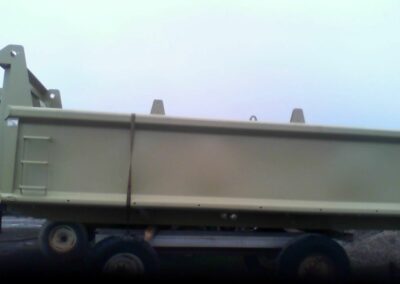 Two large olive/tan-colored steel dump truck bodies on wheeled trailers