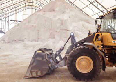 A yellow wheel loader parked in front of a large pile of road salt inside a fabric-covered storage dome