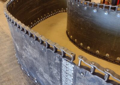 Two large rubber conveyor belt loops with heavy-duty roller chains and metal fasteners, laid out on a shop floor.