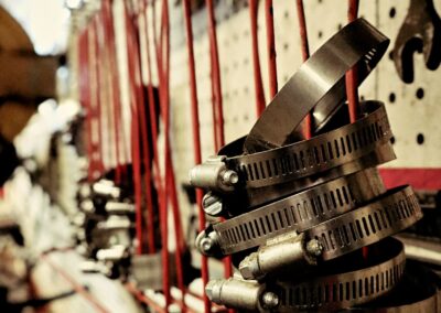 A stack of stainless steel hose clamps hanging on a red pegboard rack in a workshop, with more clamps and tools visible in the background.
