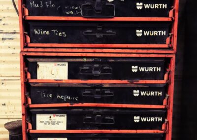 A red Würth multi-drawer parts cabinet in a workshop, with drawers hand-labeled for items like wire ties, mud flaps, and tire repair supplies.