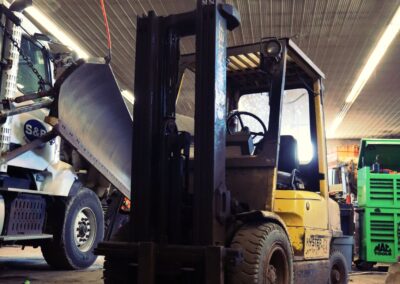 A yellow Hyster forklift parked inside a large maintenance bay alongside an S&B truck and a green MAC Tools chest.