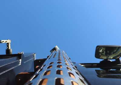 Low-angle upward view of a perforated chrome exhaust stack on a blue heavy-duty truck cab against a clear blue sky.