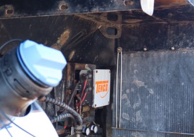 Close-up of the underside of a winter maintenance truck showing a Tenco electrical junction box, wiring harness, and spreader components with salt residue visible.