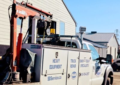 S&B Services service truck with a mechanics body and Axilift crane parked outside their shop building on a clear day.