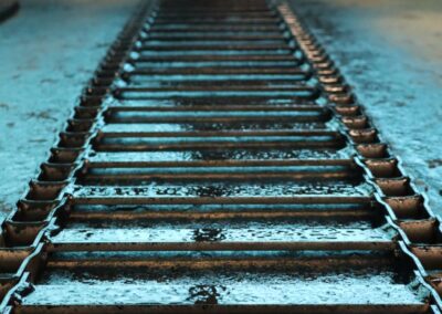 Close-up perspective view along a wet chain conveyor belt inside a spreader body, with salt residue visible on the surface.
